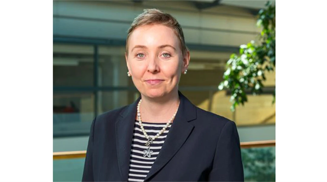 A woman with light, short hair, wearing a striped sweater and blue jacket.