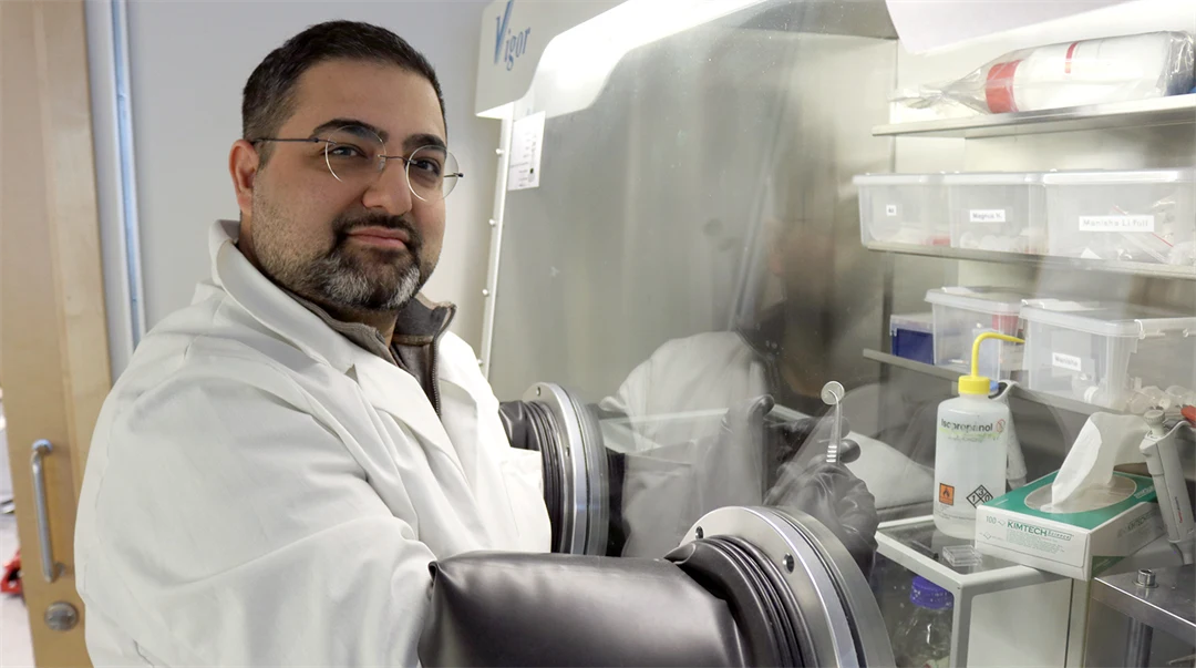 A man in a white lab coat stands in a lab.