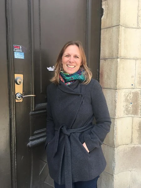 Kvinna i grå jacka och färgglad halsduk framför en brun dörr