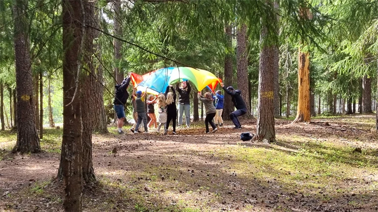 Several children holding upp a colorful sail in the forrest