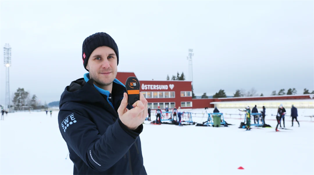 Man som visar upp en sensor stående utomhus i på en skidskyttestadion i vinterlandskap.
