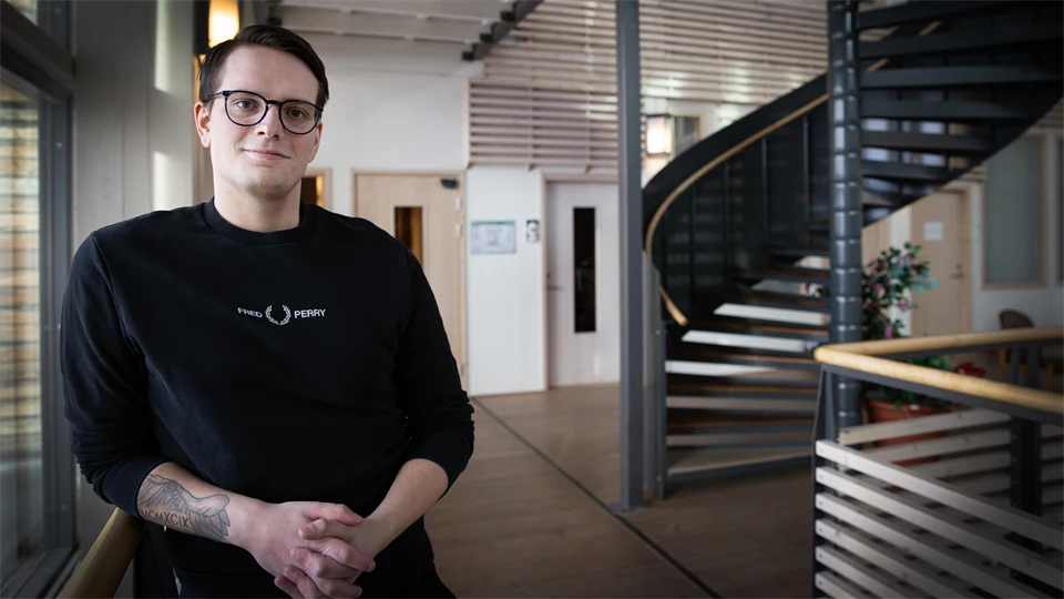 En man med svarta glasögon och svart tröja står vid ett trappräcke.