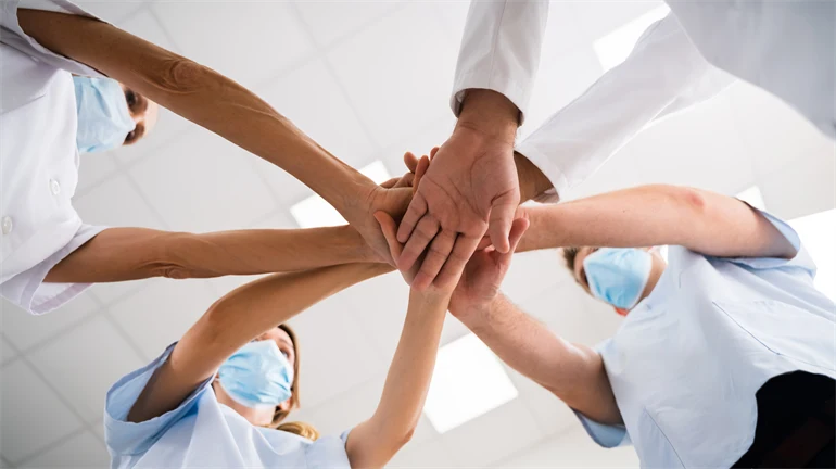 Sjukvårdspersonal står i en cirkel med händerna tillsammans i mitten.
