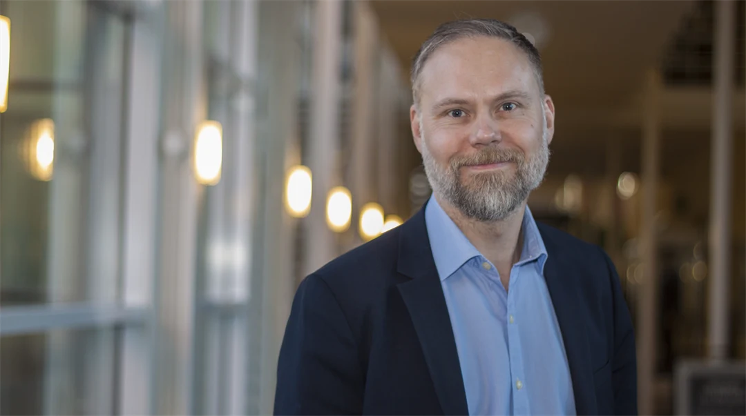 Man med skägg iklädd mörk kavaj och ljusblå skjorta