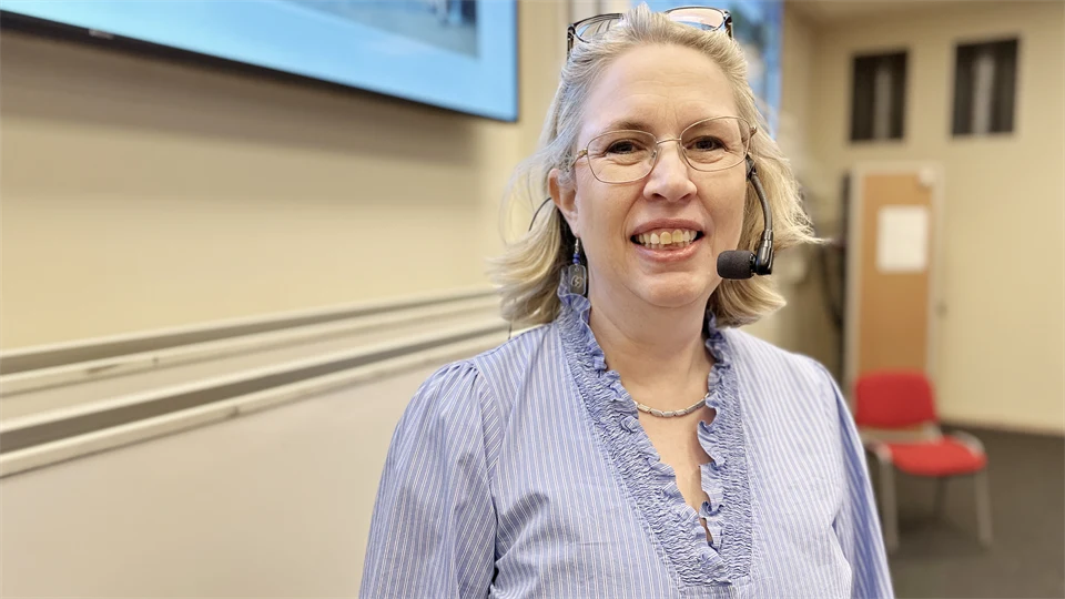 Kvinna u glasögon står i föreläsningssals.