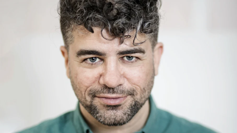 Man med grön skjorta och lockig lugg tittar intensivt in i kameran.