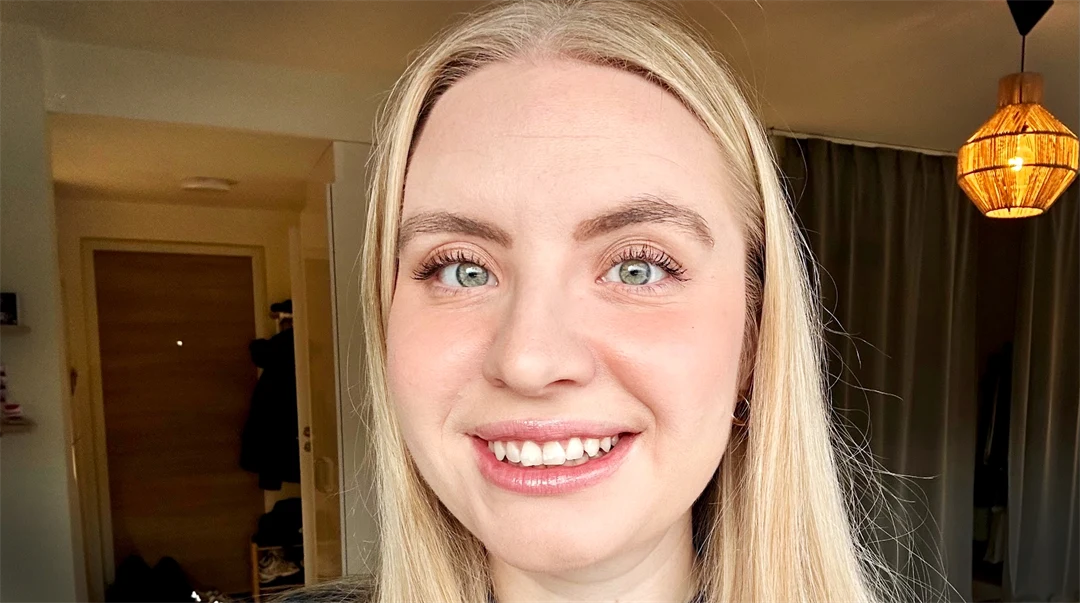 Kvinna med långt blont hår ler in i kameran.