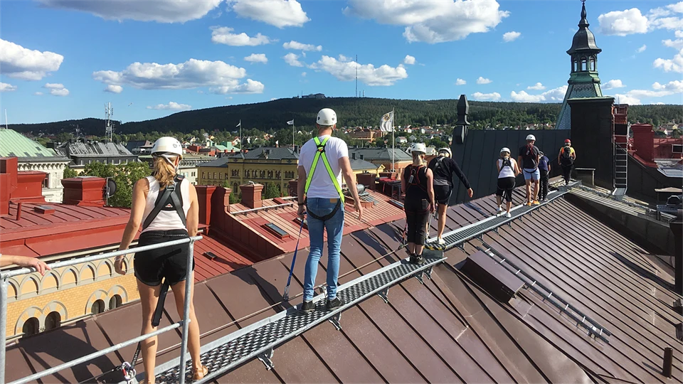  Several people in helmets walk in a row on a rooftop in a city.