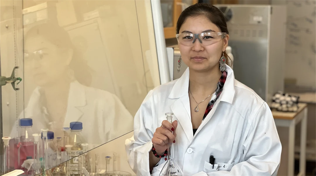 En kvinna i vit rock och skyddsglasögon står i ett laboratorium.