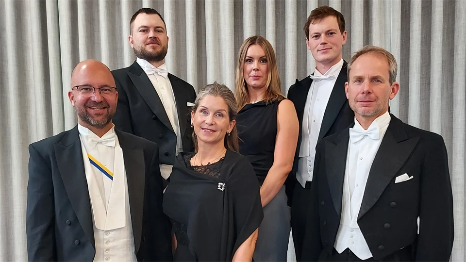 Sex finklädda personer står uppställa tillsammans. Männen i frack, gördel och vit skjorta och kvinnorna i mörka klänningar. De ler in i kameran. 