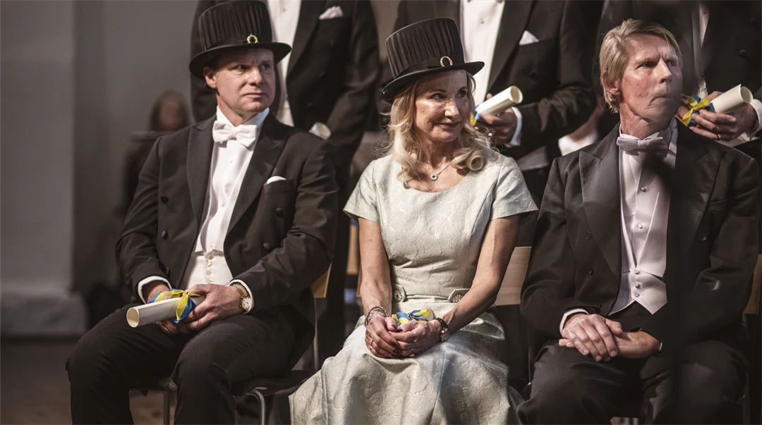 Finklädda personer med lagerkransar och doktorshattar på en scen. 