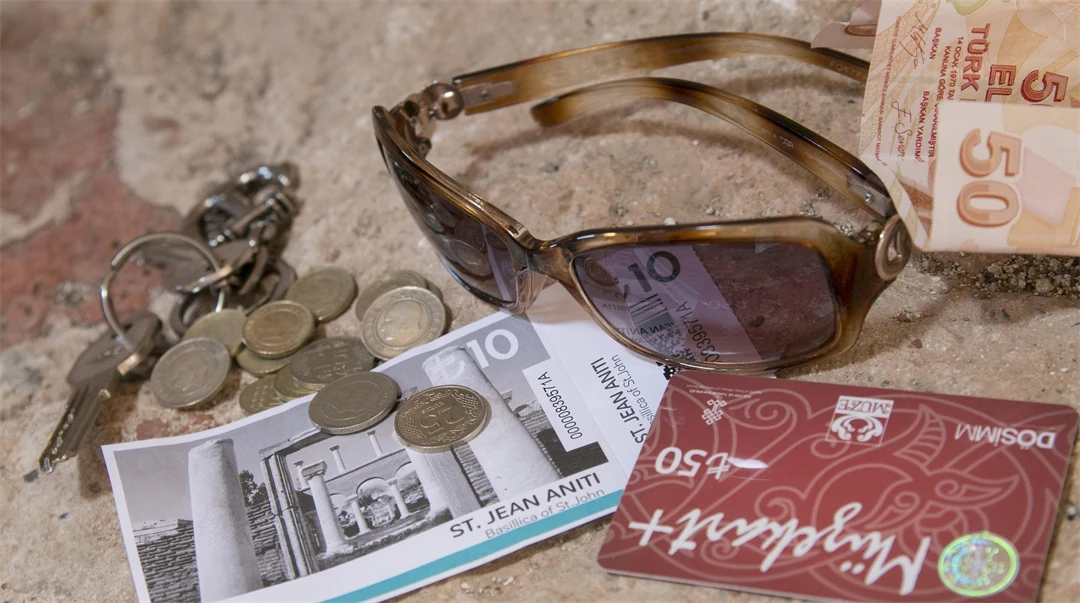 Sunglasses, money, keys and a bank card lie on a stone surface. 