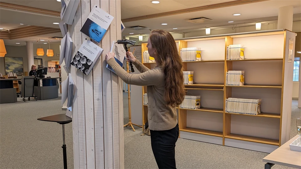 En kvinna står vid en pelare med en hammare i handen och spikar upp en avhandling på den