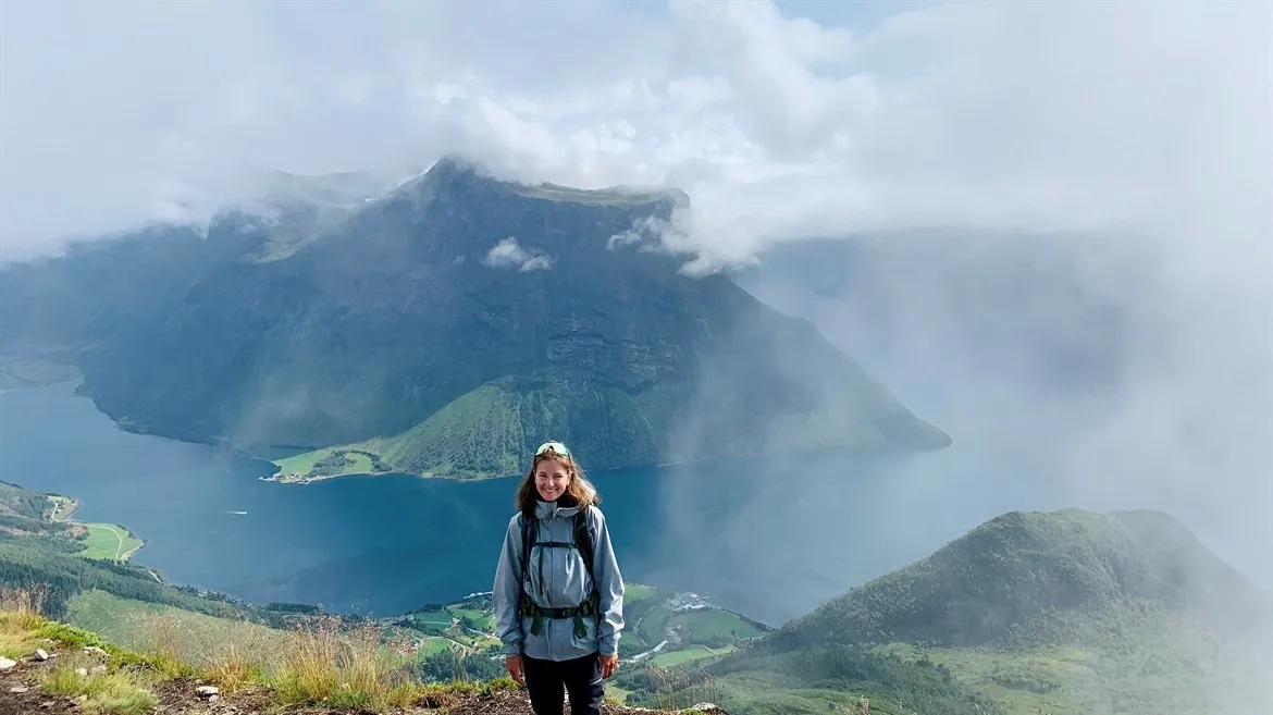 Tidigare student Amelia på ett berg med en fjord i bakgrunden