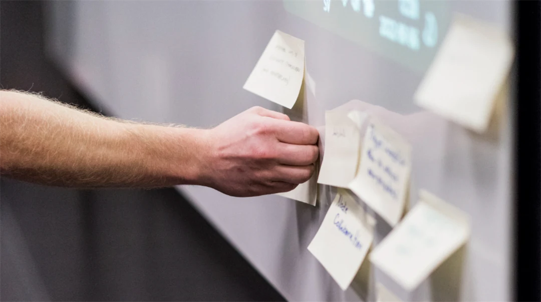A hand putting a post-it note on a board next to other post-it notes.