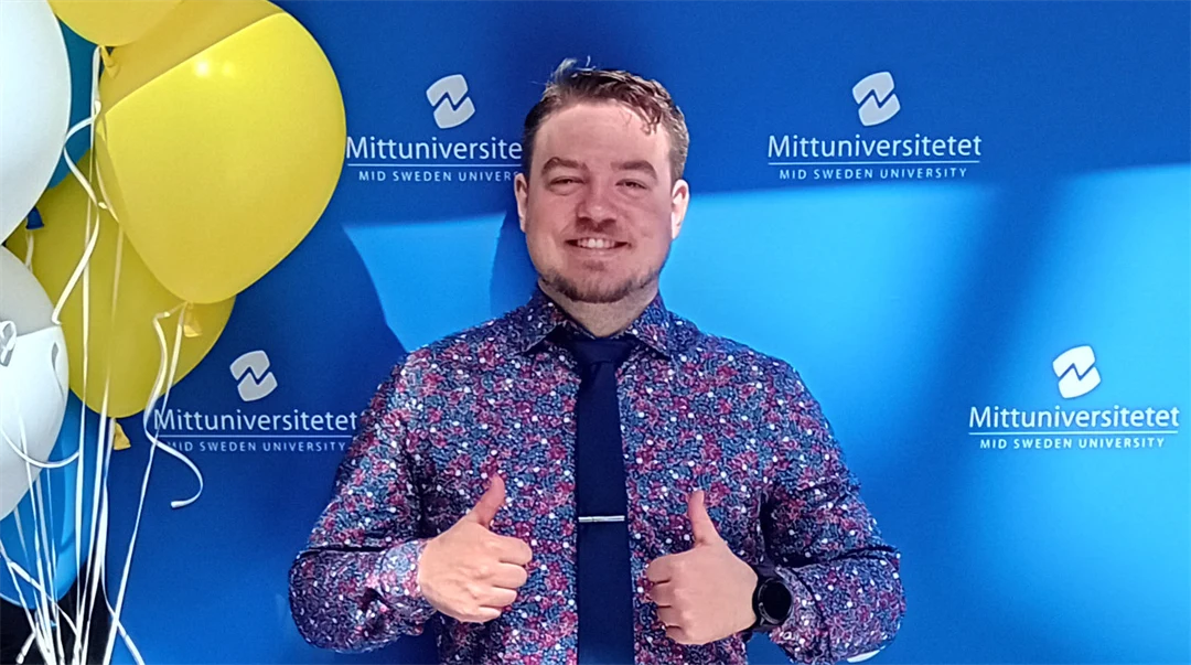 En man står framför en blå bakgrund, men några ballonger vid sidan om.