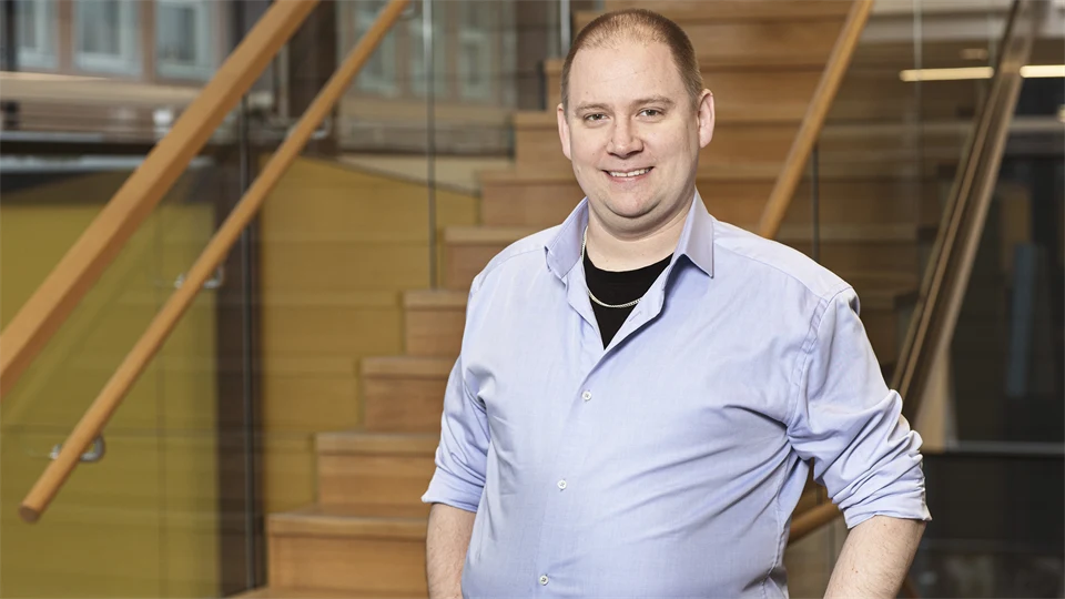 A man with a light blue shirt and short hair poses in front of the camera.