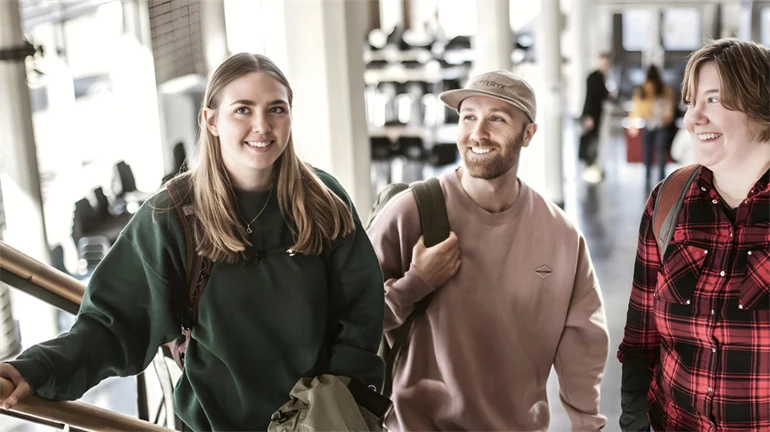 Tre unga studenter står i en trappa. De är alla glada. 