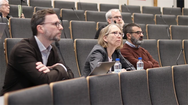 Tre personer sitter på en bänkrad i en föreläsningssal och är fokuserade framåt.