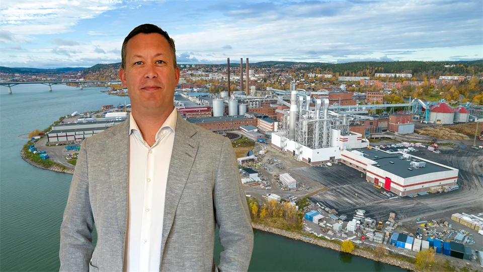 En man står framför en bild av ett fabriksområde.