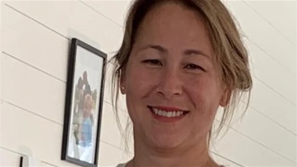 Bild på en kvinna som arbetar på folkhälsomyndigheten. Hon har uppsatt hår och ler. Bakgrunden är en vit trävägg med liggande bräder