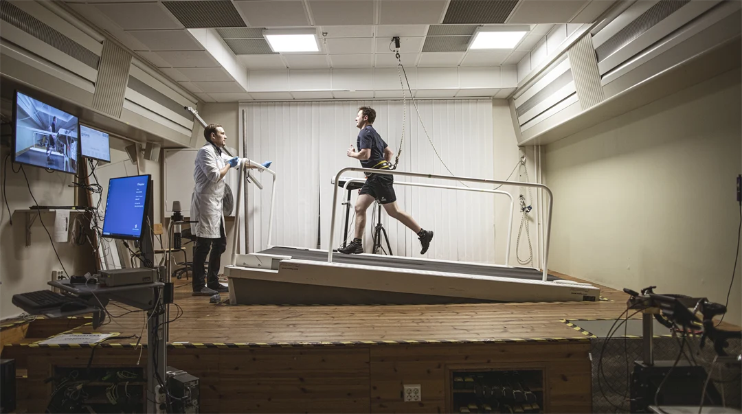 En man springer på rullband i uppförsbacke övervadad av testledare.