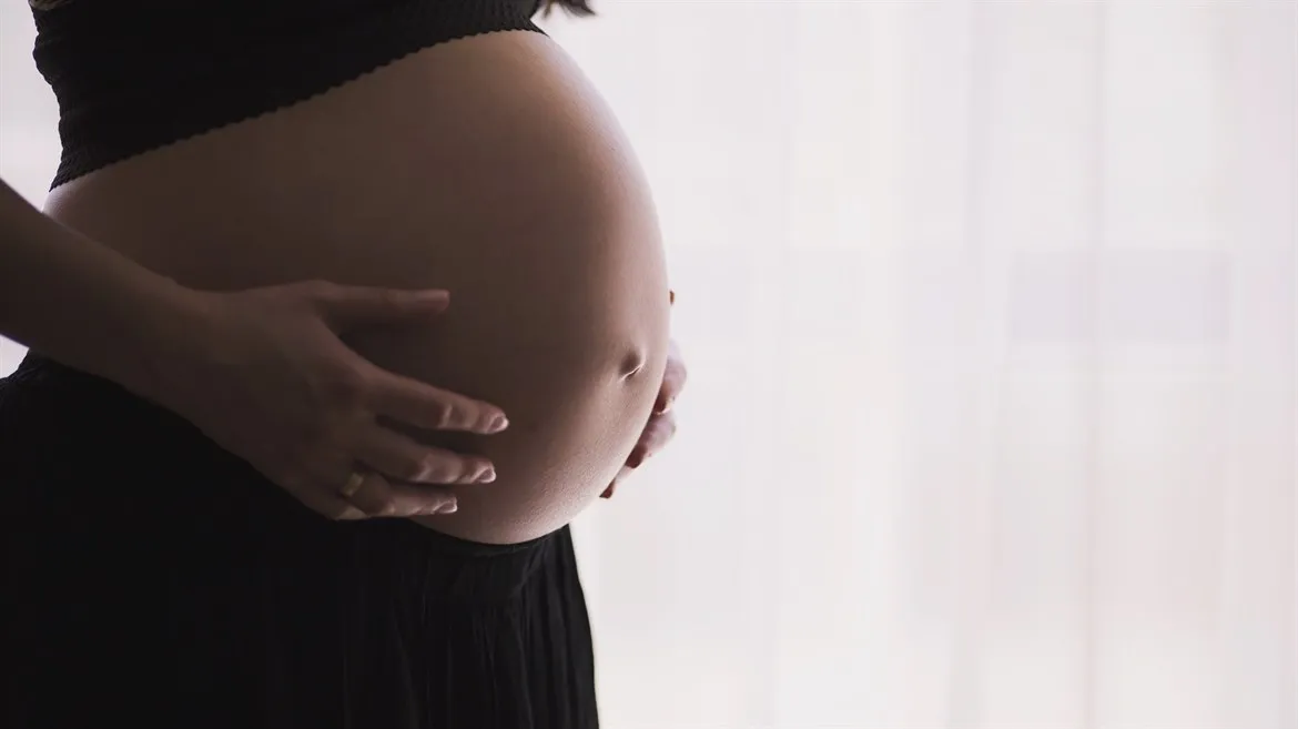 Bild på en gravid kvinna som håller i sin mage. Bilden beskuren så att man bara ser magen.