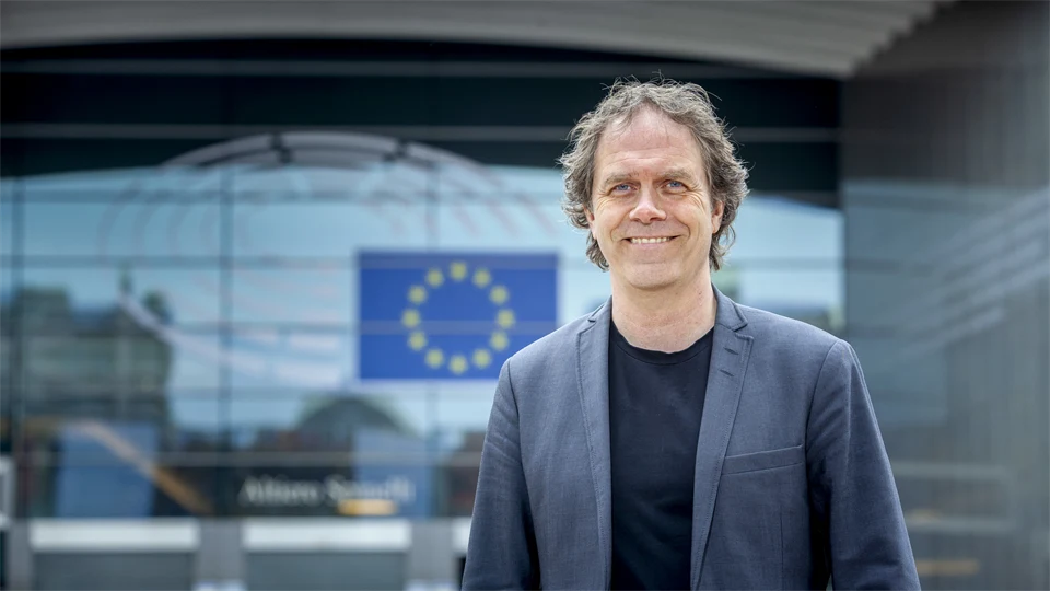 Leende man i kavaj framför glasbyggnad med EU-flagga