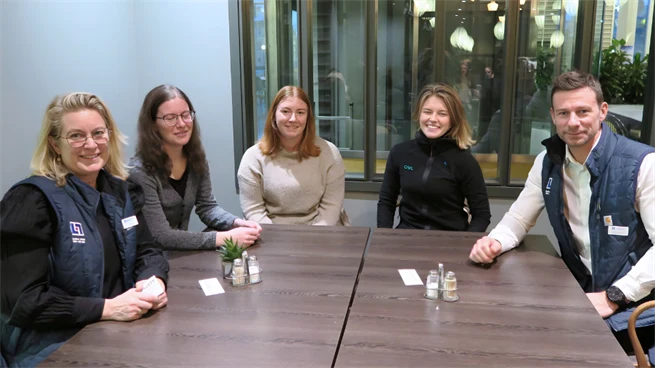 Tre kvinnliga studenter och två representanter från Länsförsäkringar sitter vid ett bord tillsammans 