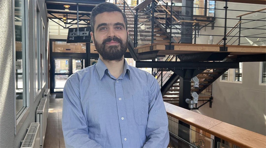 En man i blå skjorta tittar in i kameran och ler. 