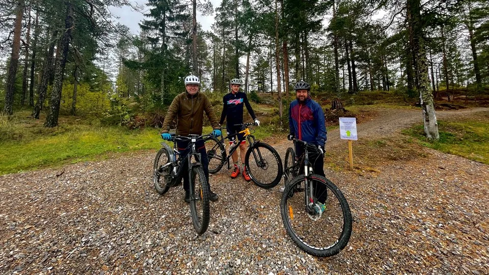 Tre personer står med varsin cykel i skogen