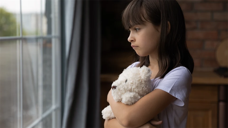 Close up, lonely little girl hugging toy, looking out of window.