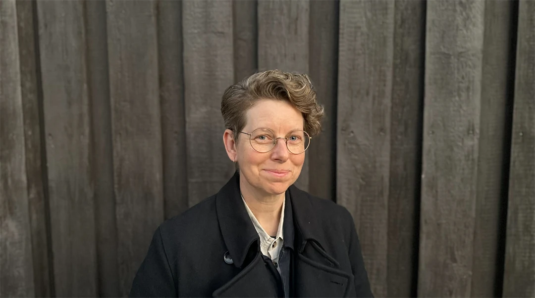 Person med blont hår och svart jacka mot en svart trävägg