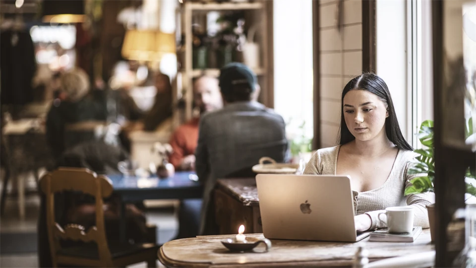 En kvinna sitter på ett kafé och jobbar vid sin dator. 