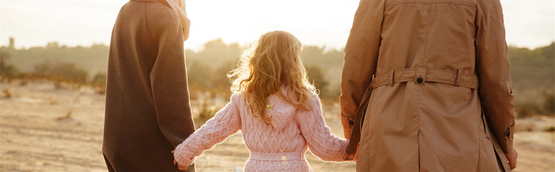 Familj i motljus, kvinna och man som håller en dotter mellan sig.