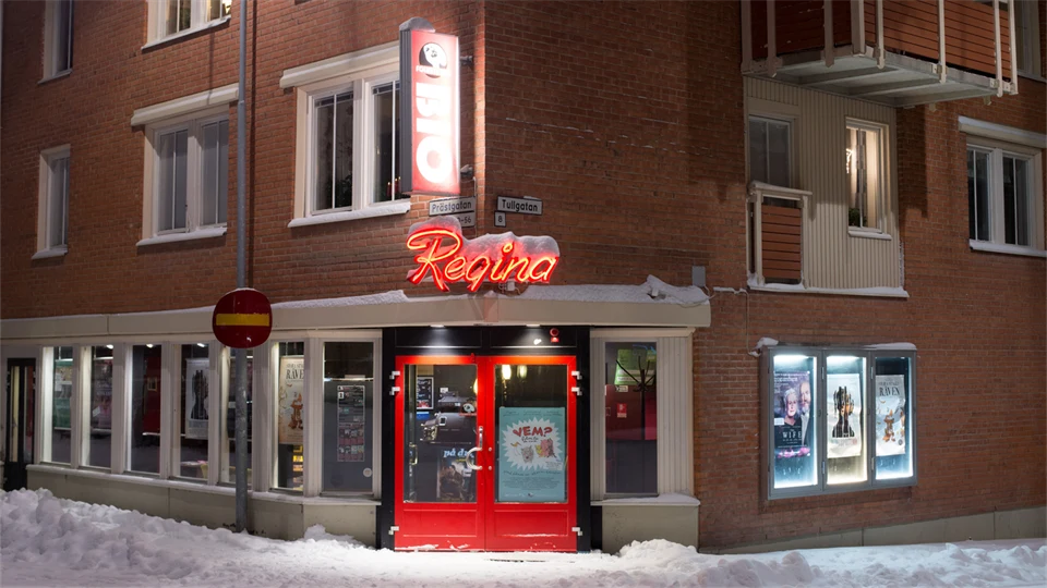 Skyltfönstret och entren till en liten biograf i Östersund. Den har röd entredörr och ovanför dörren sitter en neonskylt som visar biografens namn Bio Regina