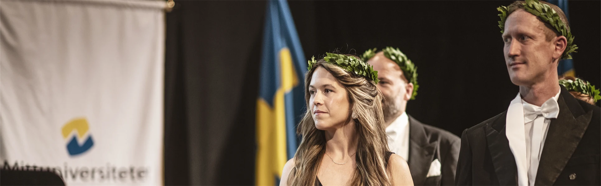 Finklädda personer med lagerkransar står på en scen med diplom i handen.