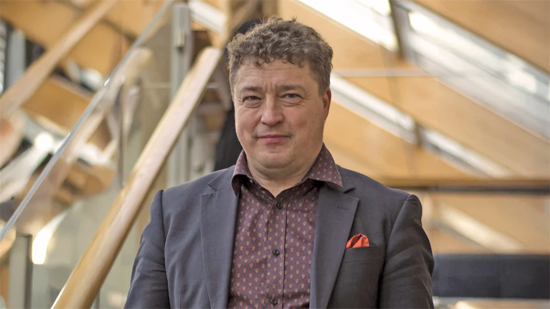 A man in a jacket looks into the camera. 