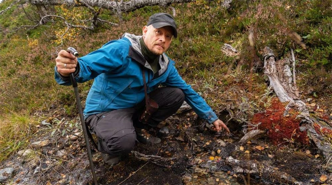 Man sitter på huk och visar en härd från en samisk kåta