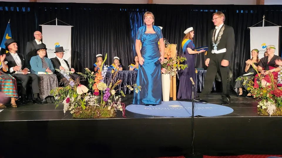 Ny profrssor i blå, glansig långklänning står på scenen under Akademiska högtiden