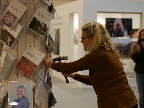 En blond kvinna håller upp en bok mot en trävägg och måttar ett slag mot den med en vacker hammare.