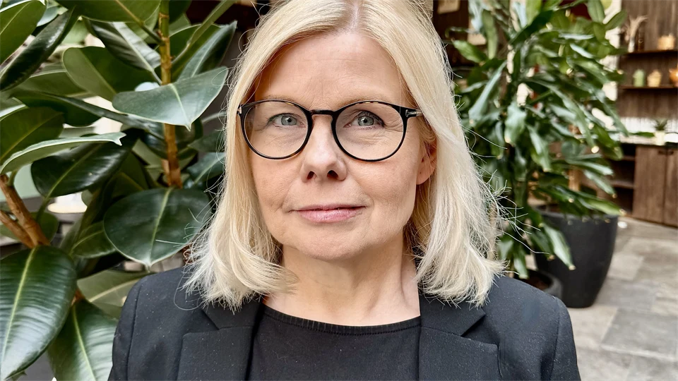 Porträttbild på ljushårig kvinna i svart kavaj och topp