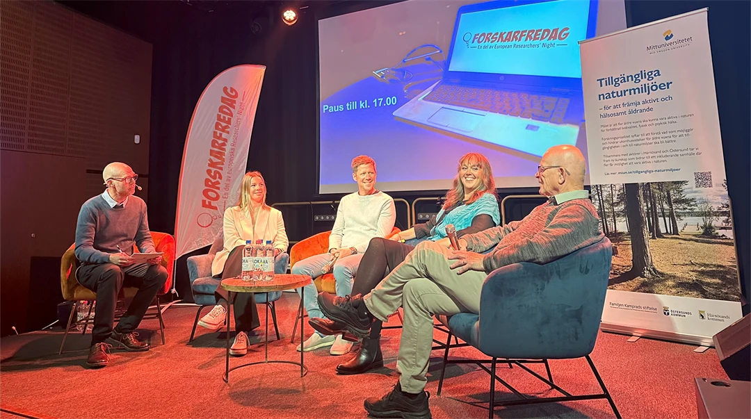 Fem personer sitter på stolar på en scen framför en skärm. 