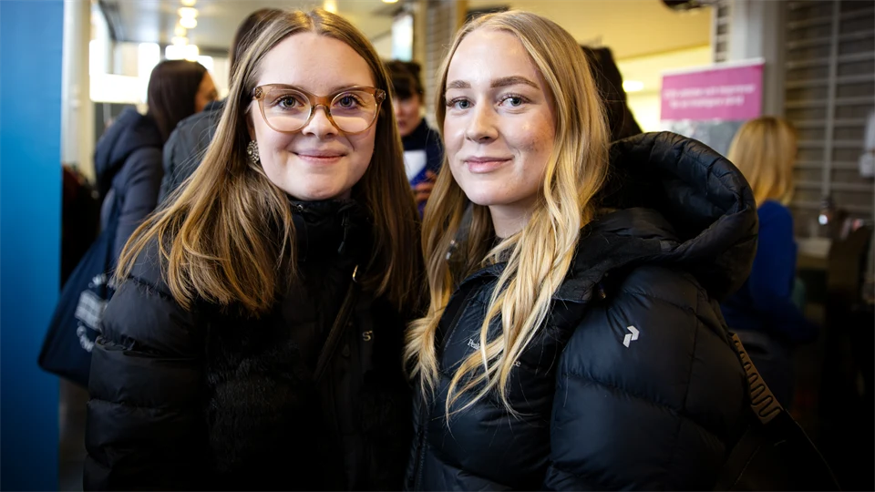 Två tjejer står bredvid varandra och tittar in i kameran.