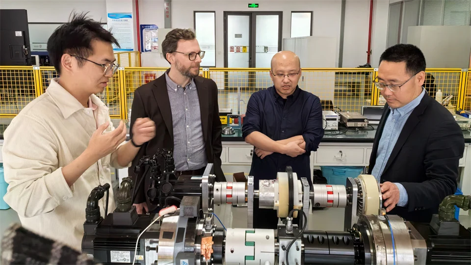  Four men stand together at equipment in a laboratory where research is being done on ball bearings.