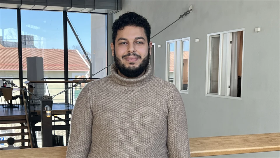  A young man in a beige sweater looks into the camera and smiles.