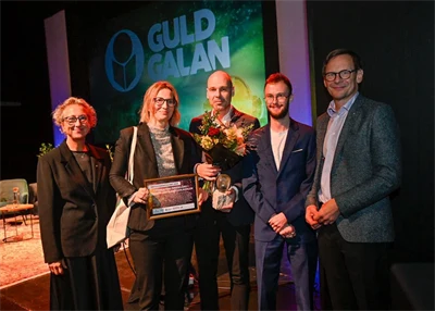 Tre män och två kvinnor med diplom och blommor i samband med prisutdelning