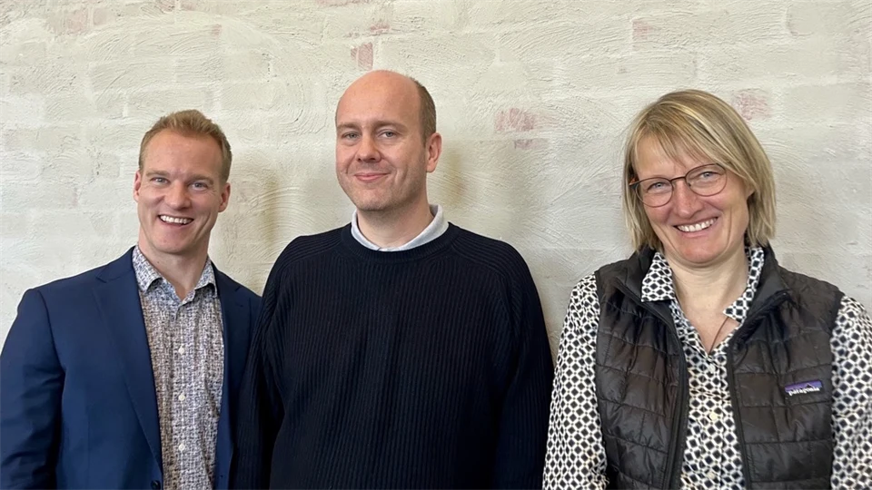 Två män och en kvinna står framför en tegelvägg. 