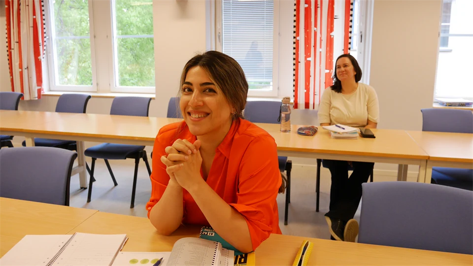 Två kvinnor sitter i en föreläsningssal med böcker framför sig.