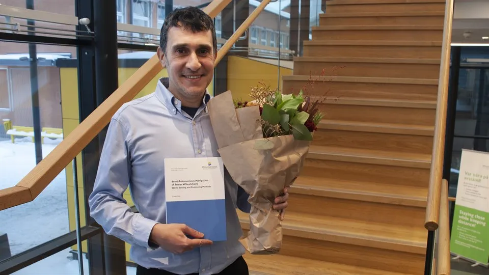 A happy man in posing infront of camera with a bouquet of flowers and his doctoral thesis.